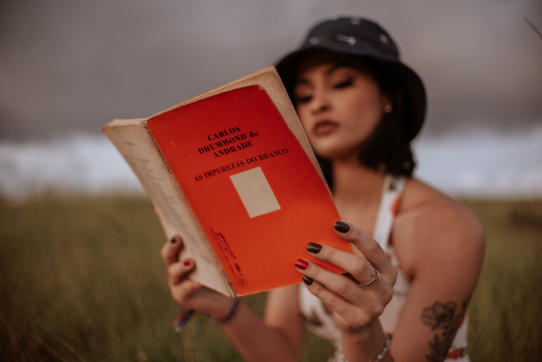Uma mulher lê um livro ao ar livre, aproveitando um tempo de lazer tranquilo em um campo gramado rural.