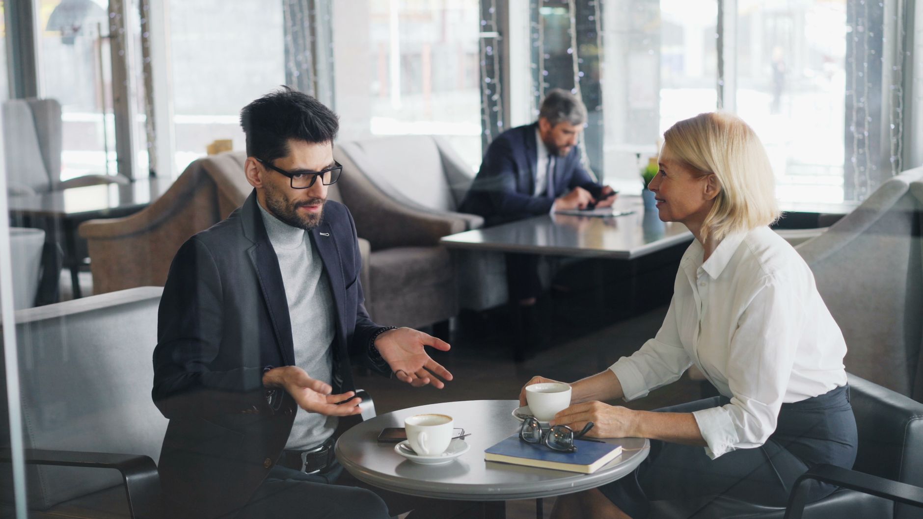 Colegas profissionais discutem trabalho enquanto tomam café em um ambiente contemporâneo de café.