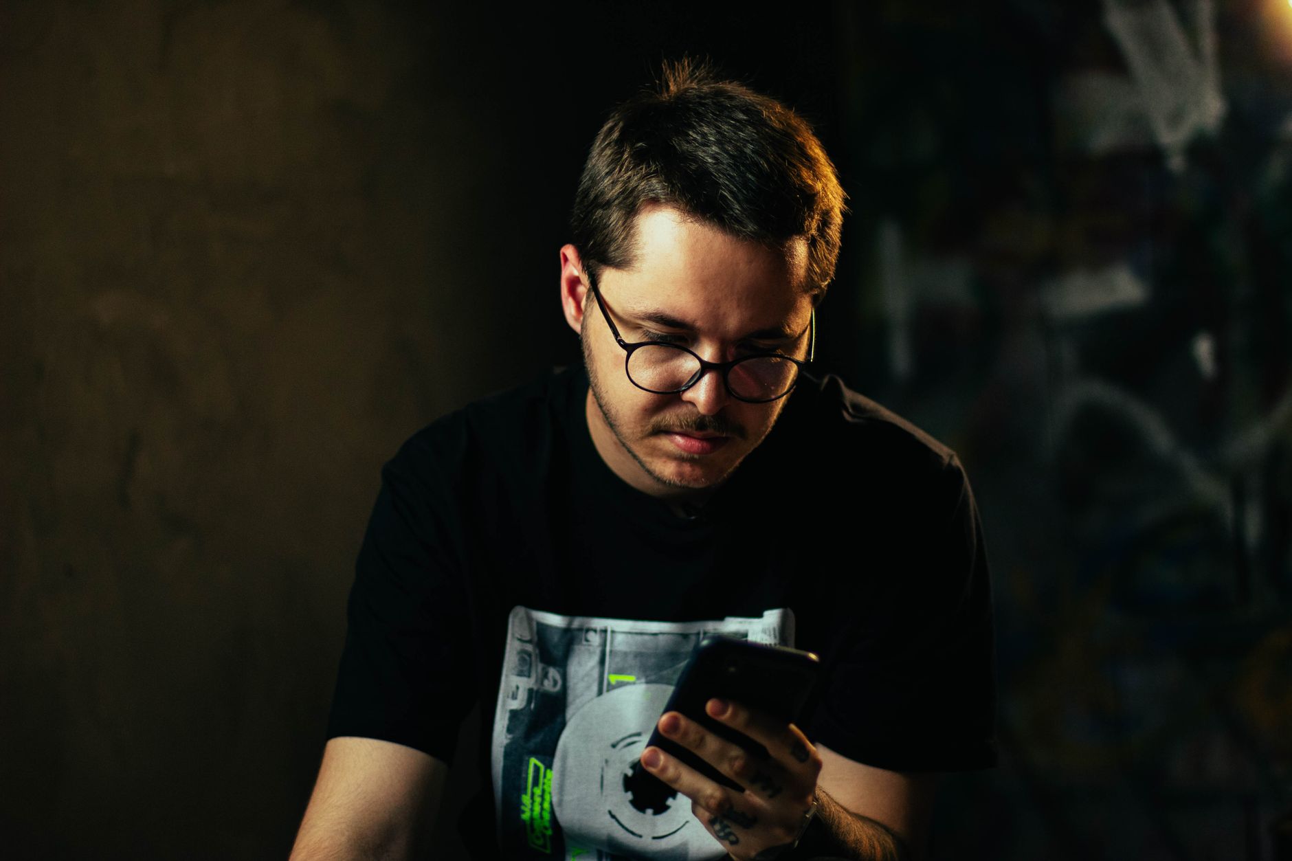 Jovem com óculos focado no smartphone em ambiente interno com iluminação atmosférica.