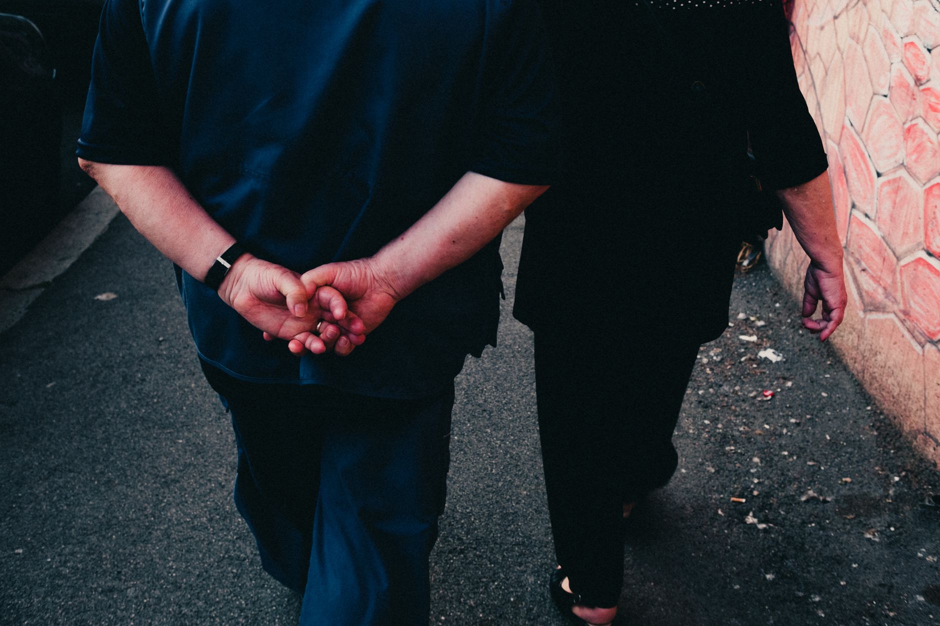 Casal de idosos andando de mãos dadas por um caminho da cidade, demonstrando afeto e companheirismo.