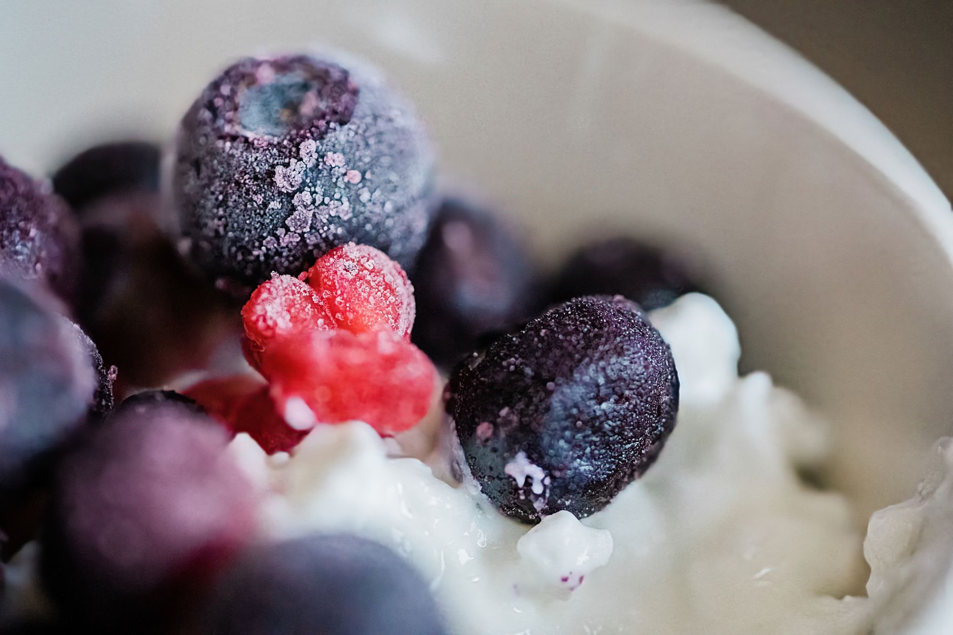 Uma imagem detalhada de frutas vermelhas congeladas sobre iogurte cremoso em uma tigela.