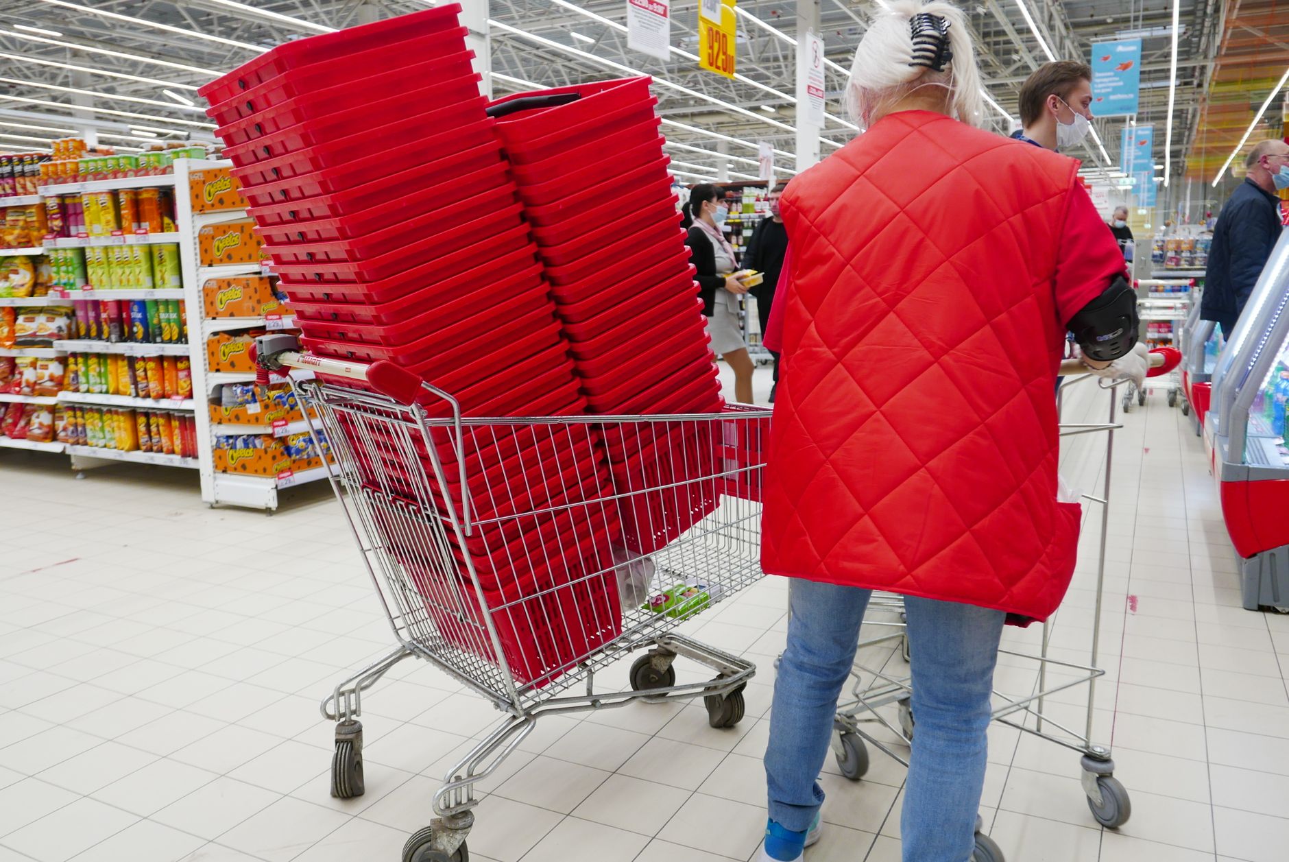 Um comprador em um casaco vermelho com cestos vermelhos empilhados dentro de um carrinho de supermercado.