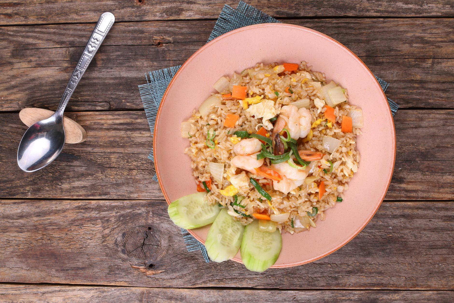Delicioso arroz frito de camarão servido com pepino em uma mesa de madeira rústica.