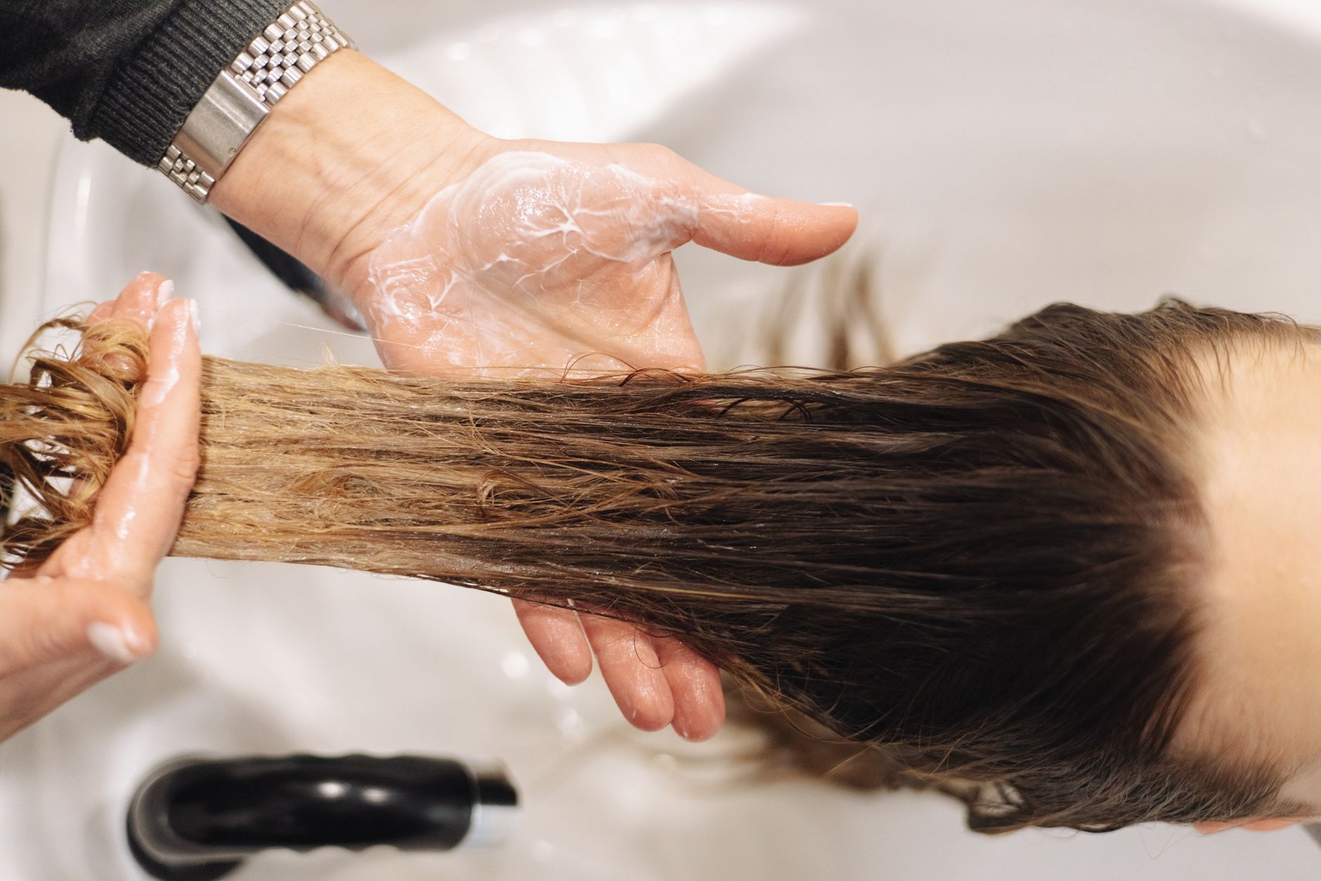 Close-up de uma lavagem de cabelo profissional em um ambiente de salão, destacando a técnica das mãos.