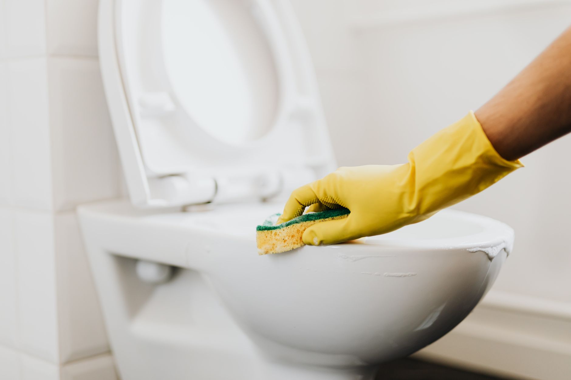 Um close de uma mão com luva amarela limpando um vaso sanitário com uma esponja, promovendo a higiene.