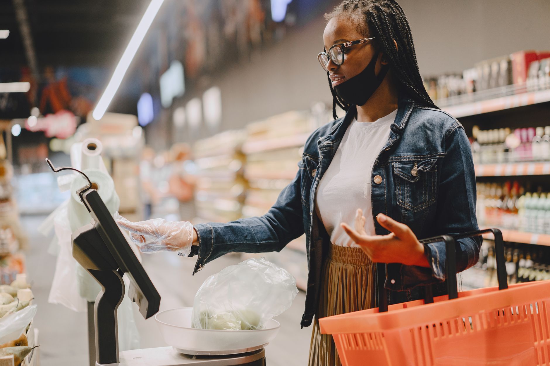 Uma mulher pesando vegetais em um supermercado usando uma balança digital com um carrinho de compras.