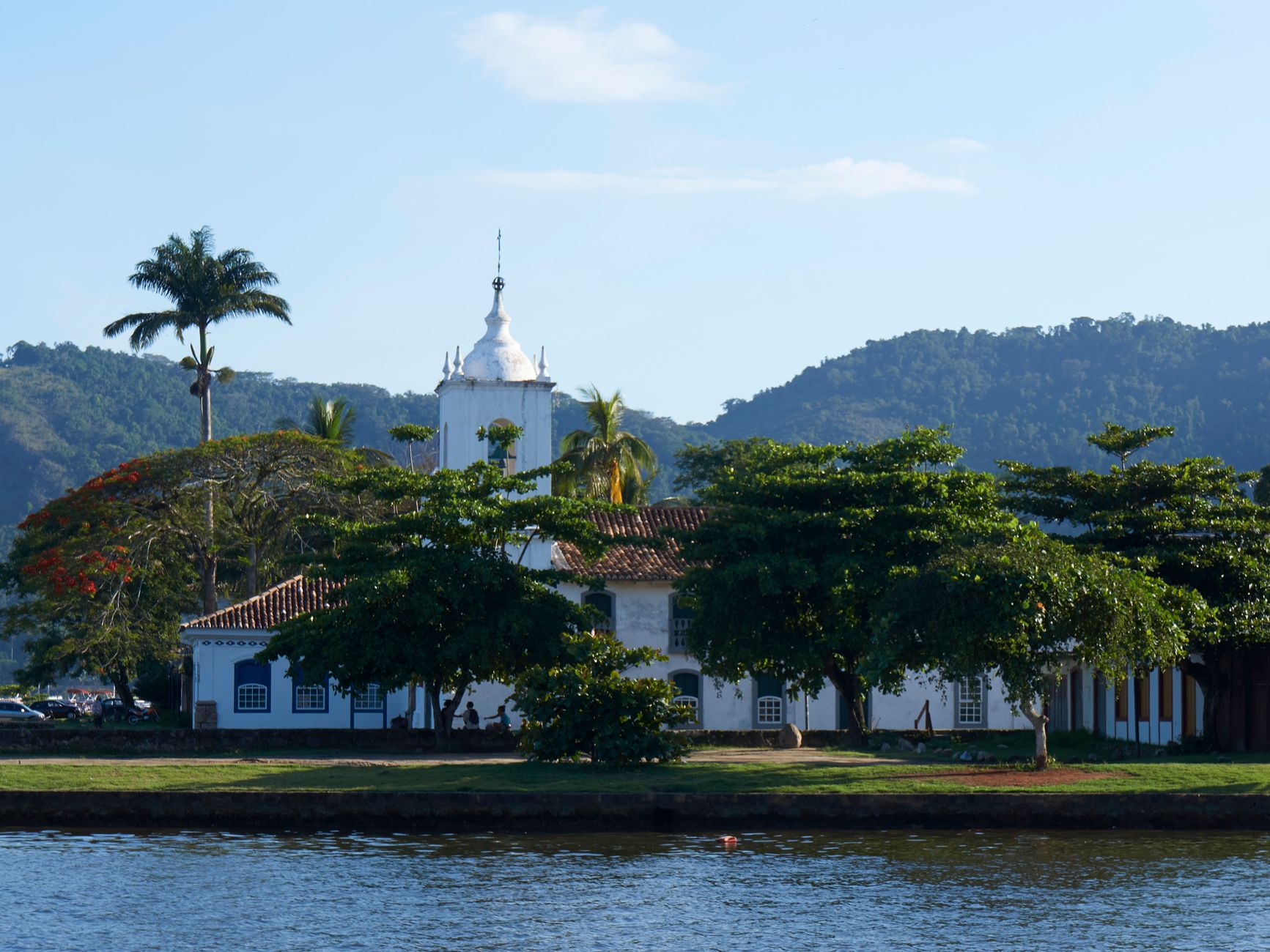 Paisagem idílica com uma igreja histórica, árvores exuberantes e um rio calmo em Paraty, Brasil.