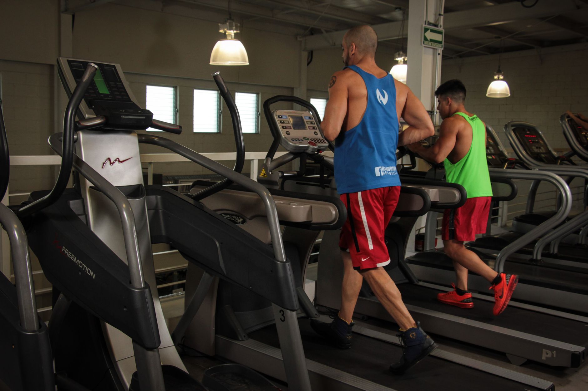 Dois homens correndo em esteiras em uma academia moderna, promovendo fitness e saúde.
