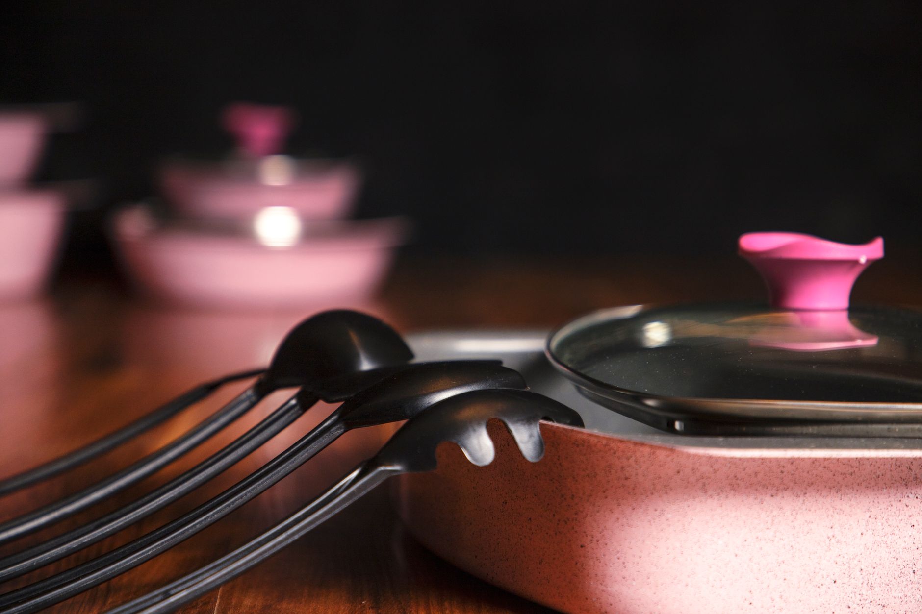 Close-up de utensílios e panelas rosas em uma bancada de madeira, enfatizando elegância e estilo.