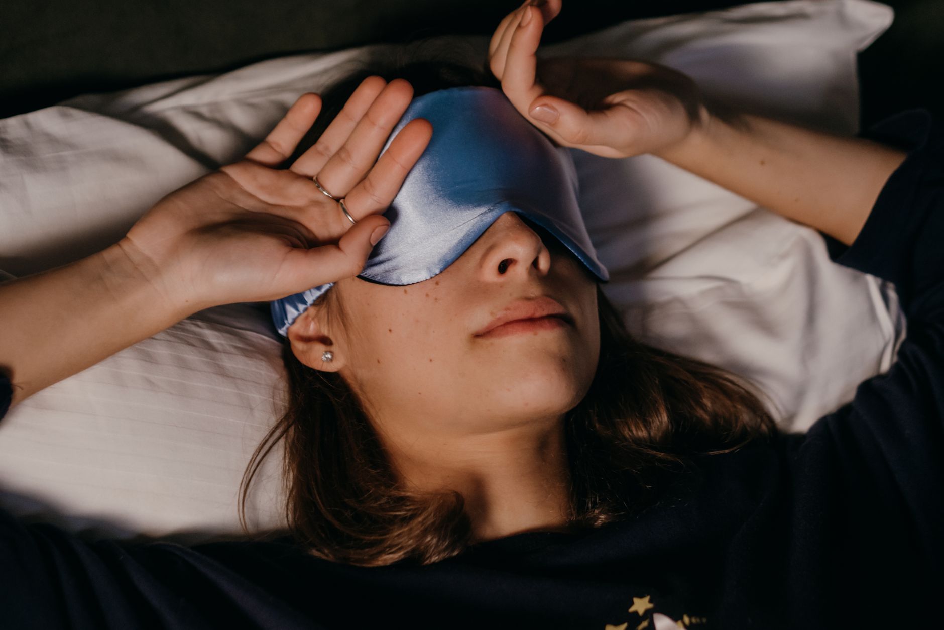 Uma mulher descansando pacificamente com uma máscara de dormir em um ambiente interno aconchegante.