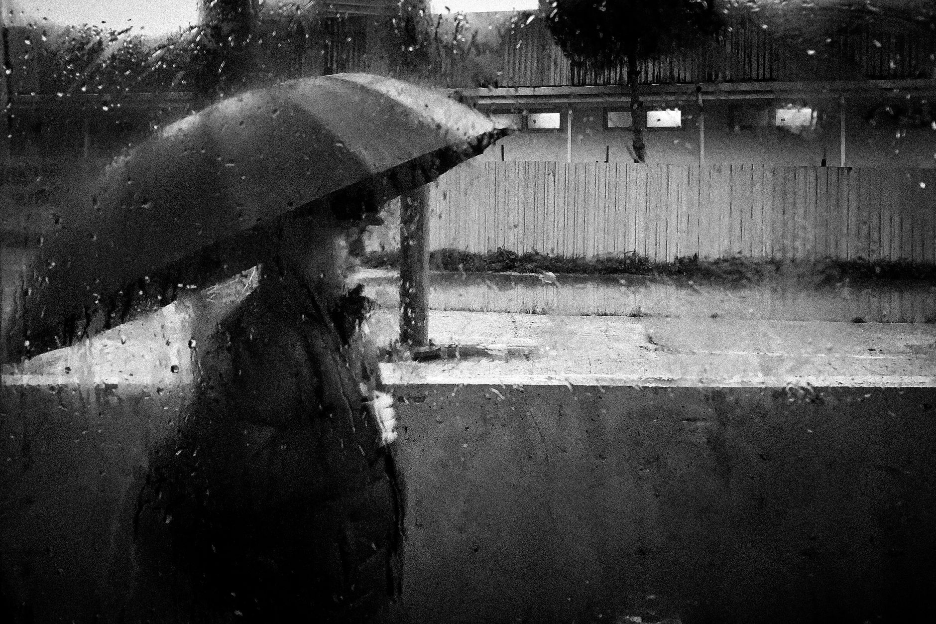 Foto em preto e branco de uma pessoa caminhando com um guarda-chuva em um dia chuvoso.