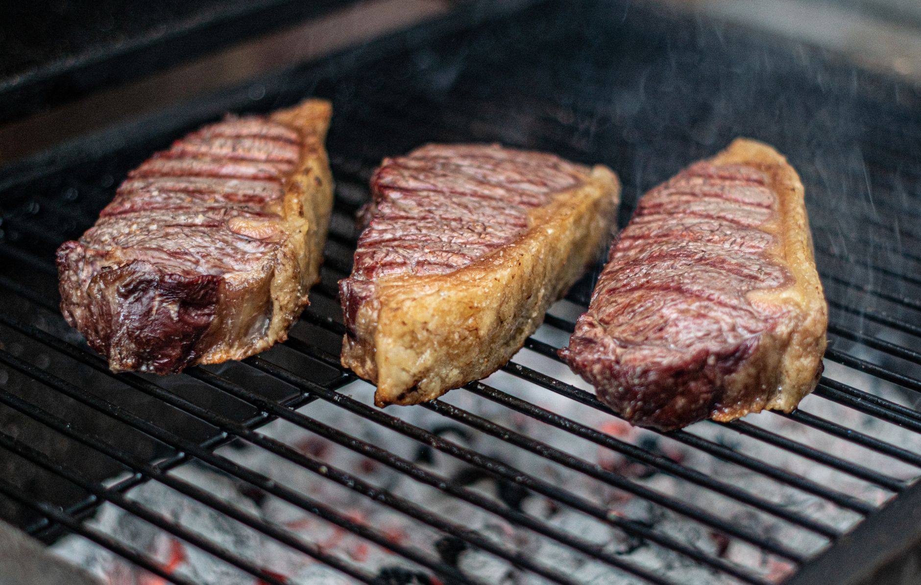 Close-up de três suculentas carnes grelhando em um churrasco, perfeitas para um cookout de verão.