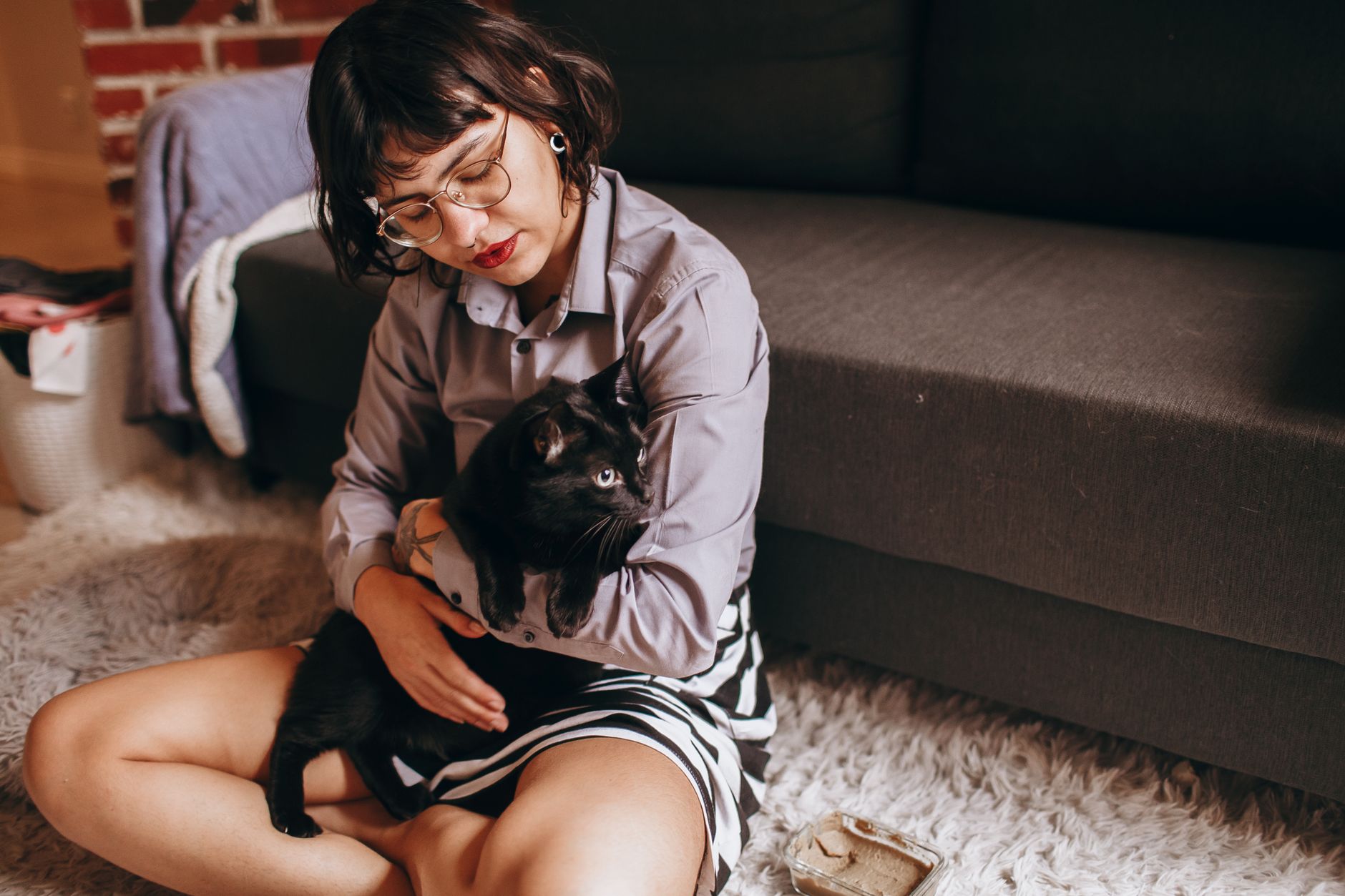 Mulher segurando um gato preto enquanto está sentada em um tapete aconchegante dentro de casa.