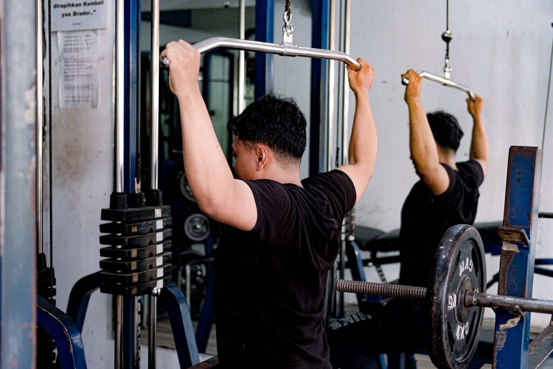 Homem adulto utilizando uma máquina de puxada dorsal em uma academia, com foco em treinamento de força.