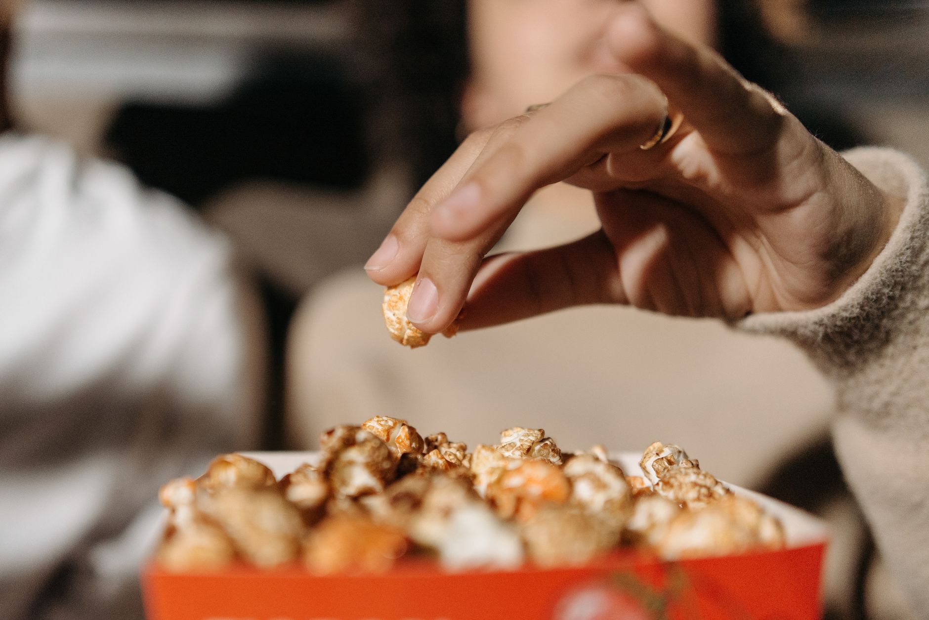 Uma mão alcança um pedaço de pipoca em um ambiente de cinema, criando uma atmosfera aconchegante.