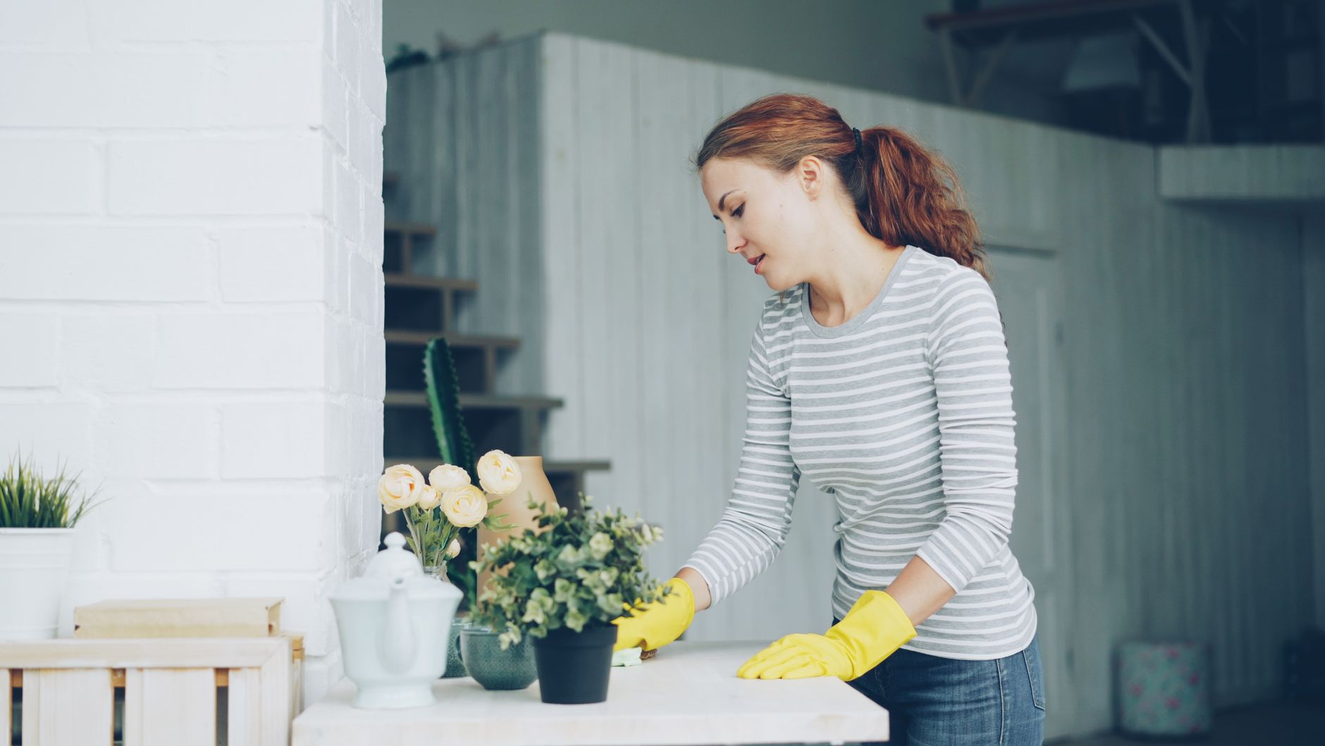 Mulher cuidando de plantas internas em um ambiente moderno, usando luvas amarelas para jardinagem.