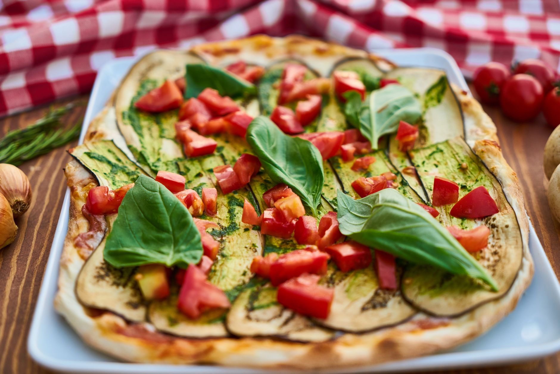 Close-up de uma vibrante pizza italiana coberta com berinjela fresca, manjericão e tomates.