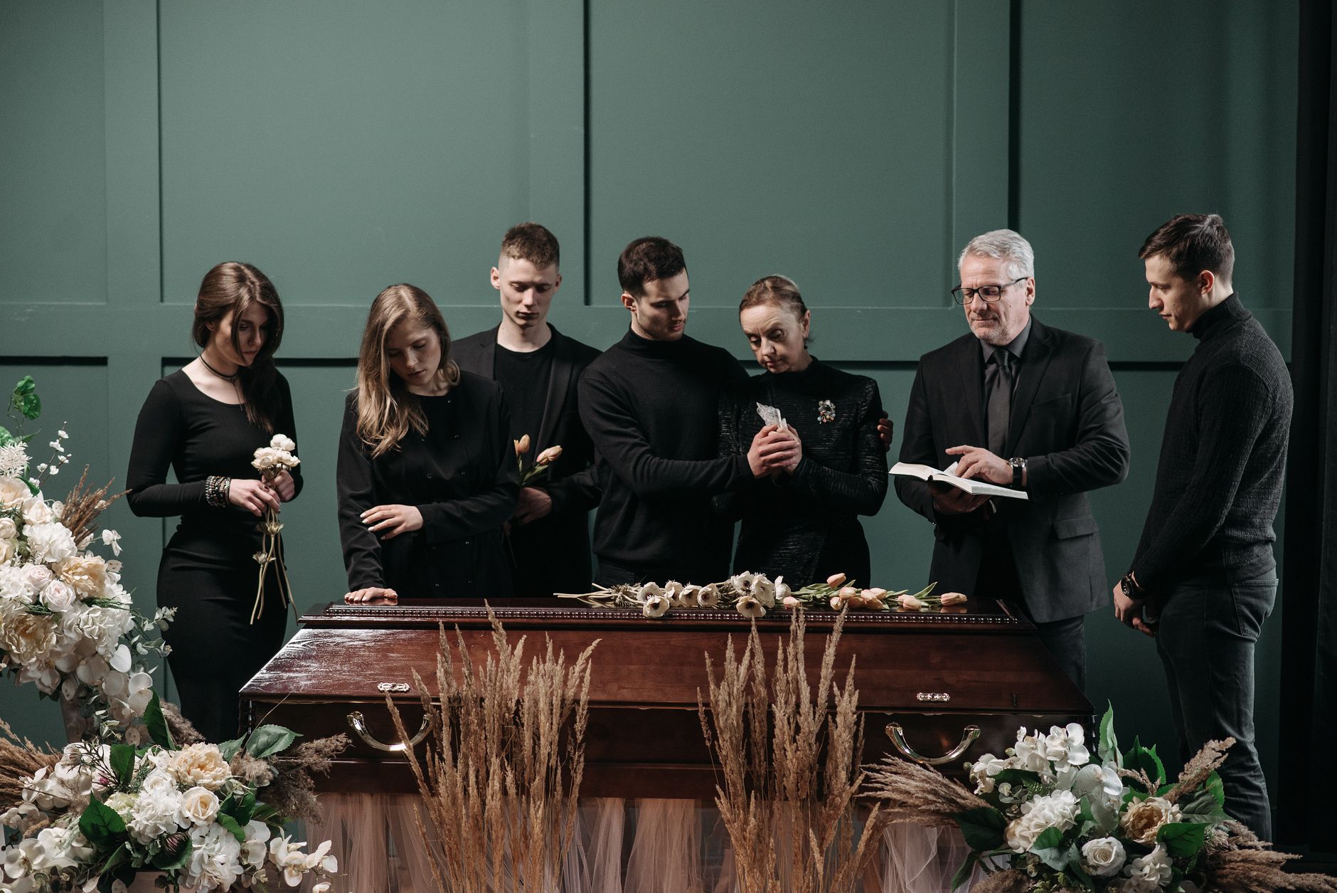 Uma reunião fúnebre com adultos em um ambiente interno solene ao redor de um caixão, simbolizando perda e lembrança.