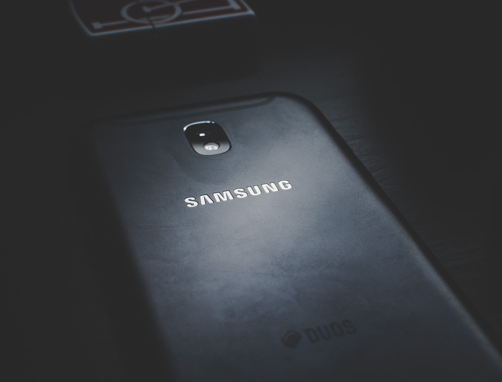 Visão detalhada de um smartphone sobre uma superfície de madeira escura destacando seu logo.
