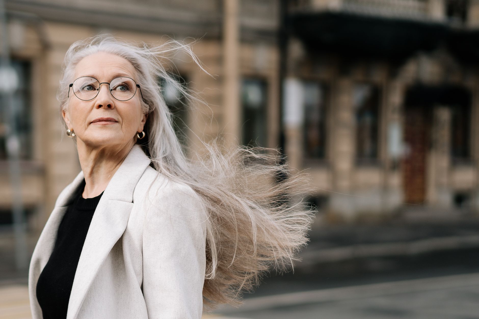Estilosa mulher idosa com cabelo solto e óculos caminhando em um ambiente urbano arejado.