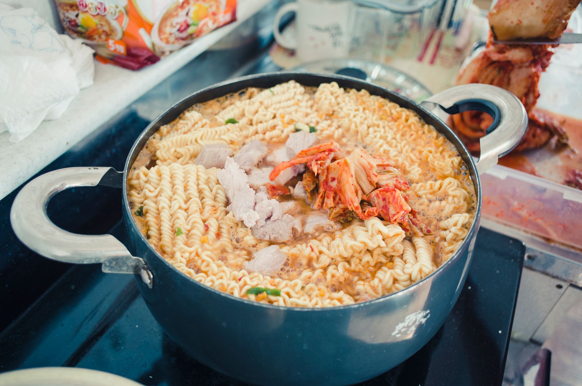 Deliciosa sopa de macarrão com kimchi cozinhando em uma panela, apresentando macarrão vibrante e ingredientes saborosos.