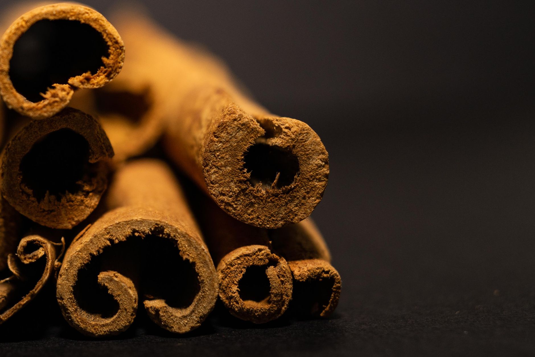 Close de bastões de canela aromática em fundo preto, destacando textura e profundidade.