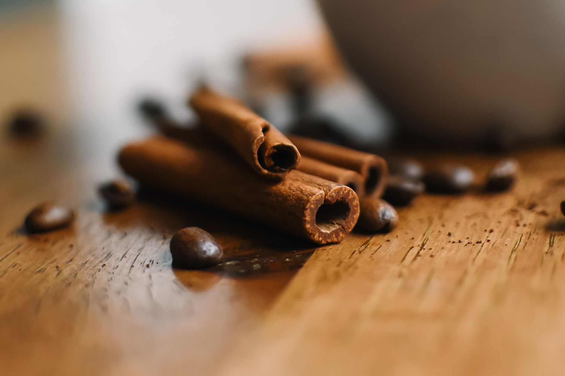 Bastões de canela aromáticos com grãos de café espalhados sobre uma superfície de madeira.