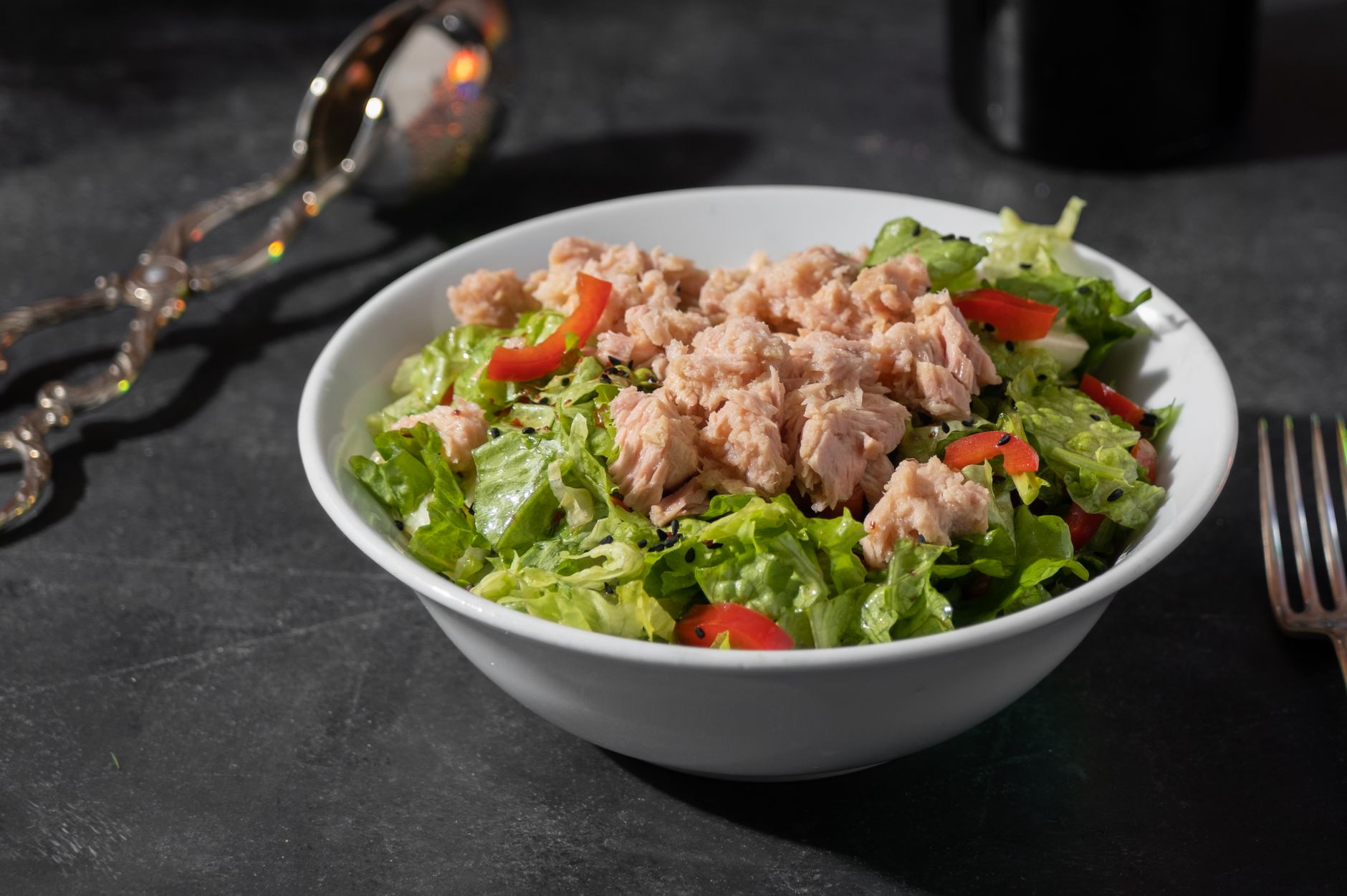 Um close de uma salada de atum fresca, com alface e tomates em uma tigela branca sobre uma superfície escura.